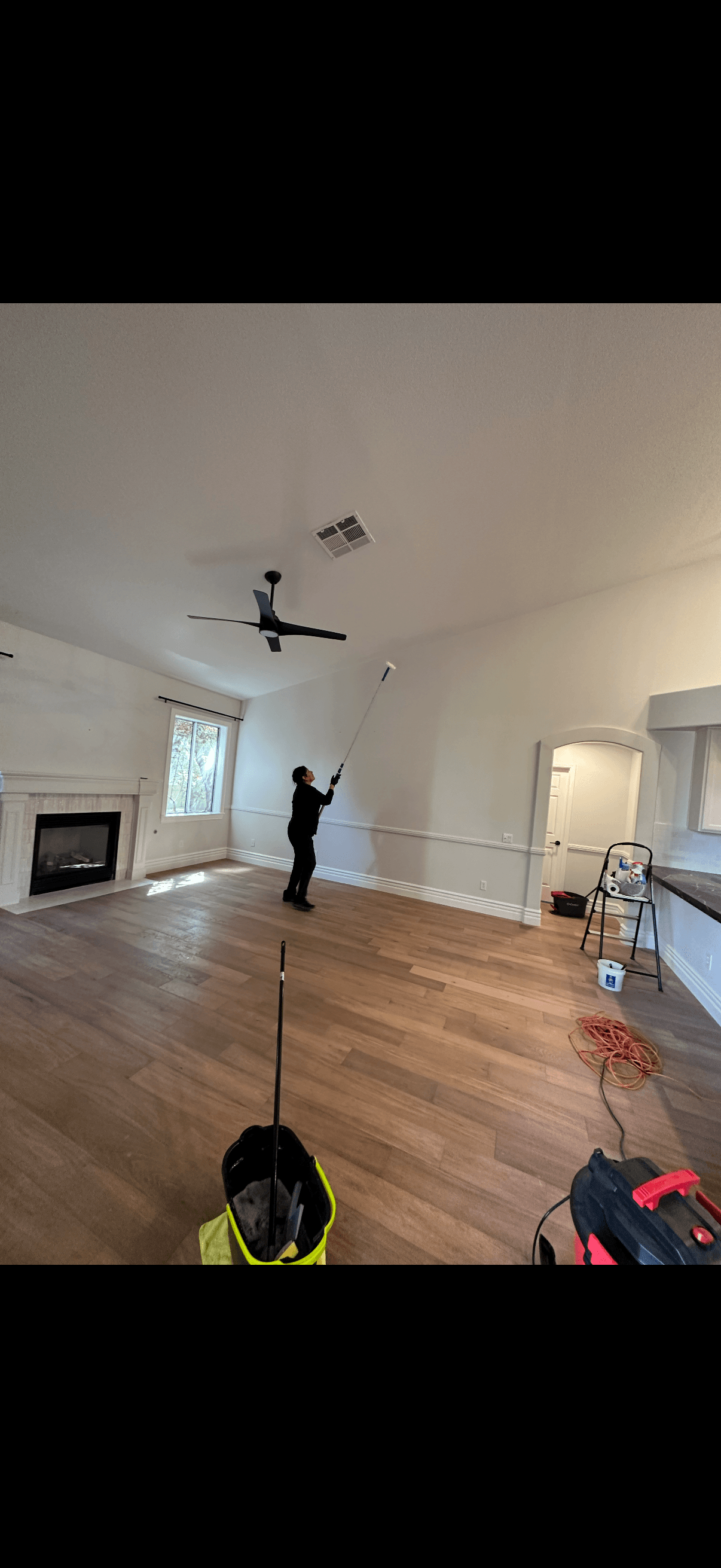 Vital Cleaning team member using an extension duster to clean high walls in a living room
